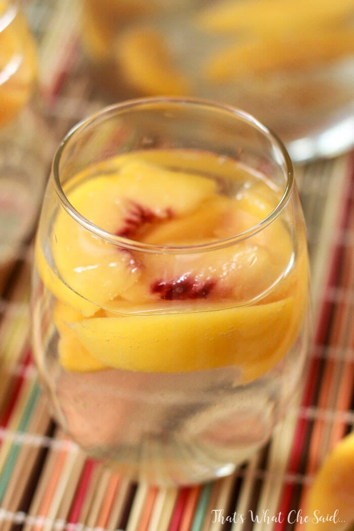 The Best White Peach Sangria Recipe - White Wine Peach Sangria in a Wine glass with floating peaches on top