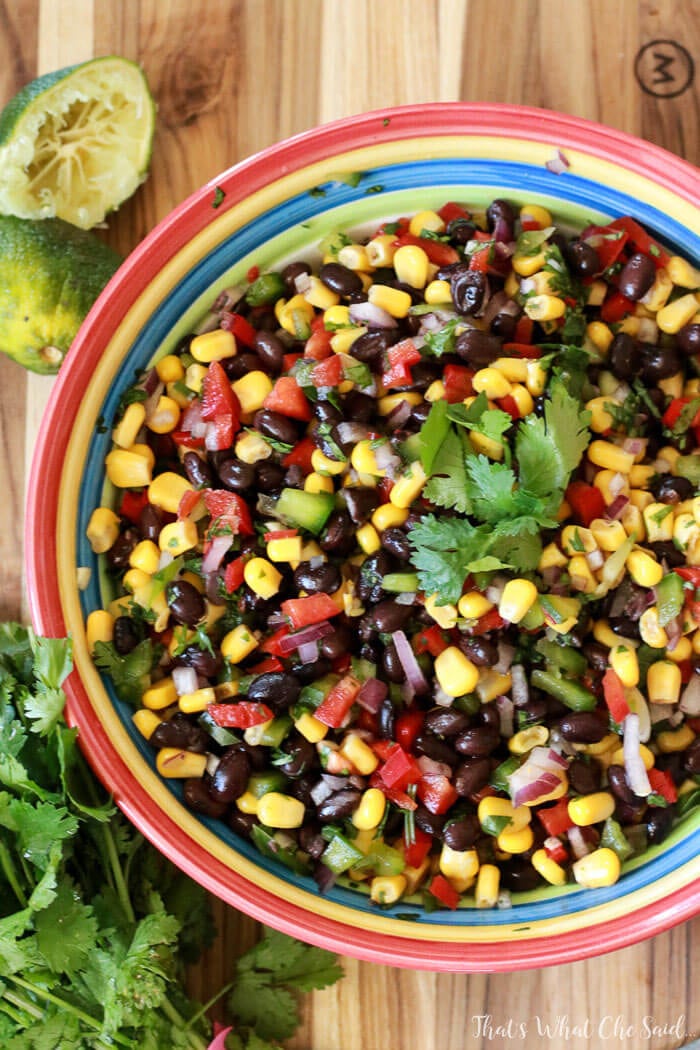 Top view shot of bowl full of Corn & Black Bean Salsa. Fresh squeezed limes and cilantro garnish