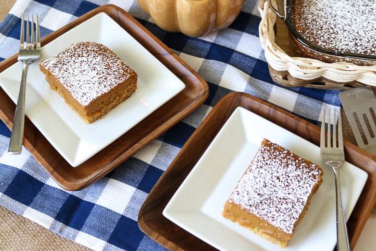 Two square plates with cut pieces of pumpkin gooey butter cake with powdered sugar topping