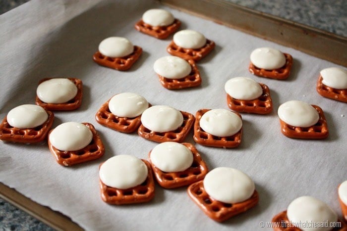 Parchment lined sheet pan with square pretzels in a single layer with a white candy melt on top