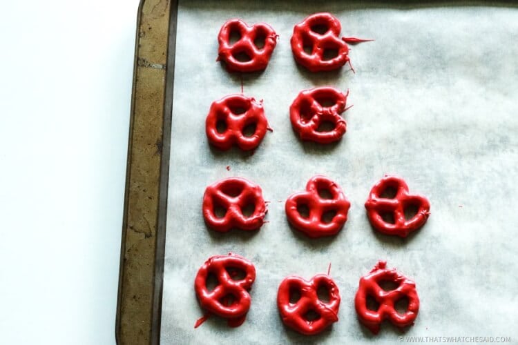 Pretzels dipped in red candy melts cooling on a parchment lined cookie sheet