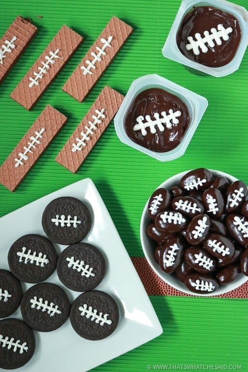 Four different foods made to look like footballs with icing laces; chocolate wafer cookies, chocoalte covered almonds, Oreo cookies and fudge pudding snack packs. 