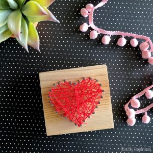 Small block of wood with nails and red string in a heart shape