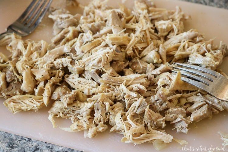 Chicken thighs that were cooked in the instant pot and now shredded on a cutting board with 2 forks. 