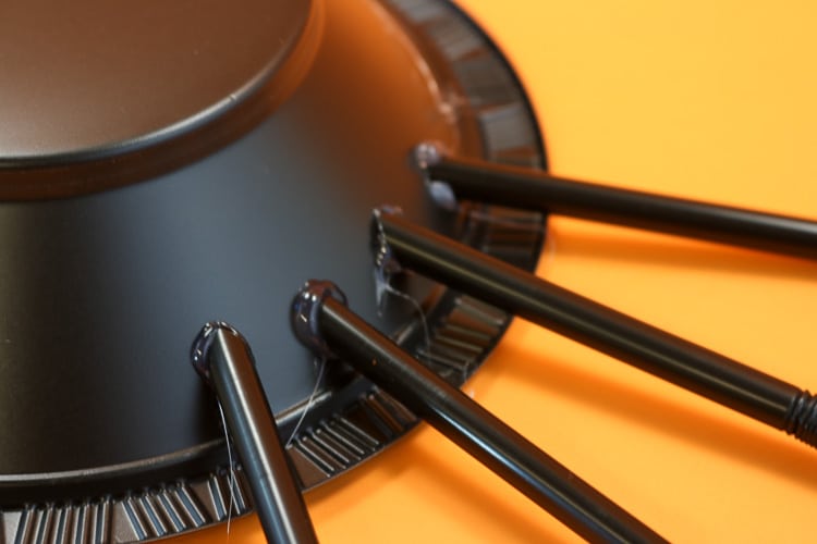 Showing hot glued straws onto plastic bowl as spider legs