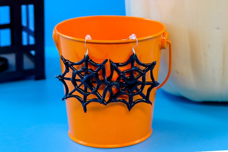 Completed hot glue spider web earrings hanging on a small orange bucket