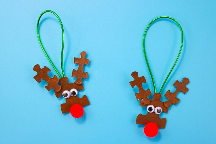 Two upcycled reindeer ornaments made from puzzle pieces and googly eyes and red pompoms