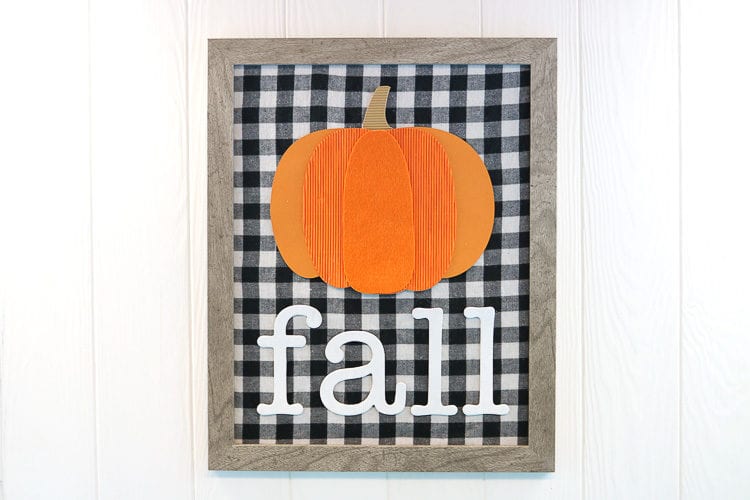 Framed sign with buffalo plaid fabric, a mixed media pumpkin and the word fall in chipboard