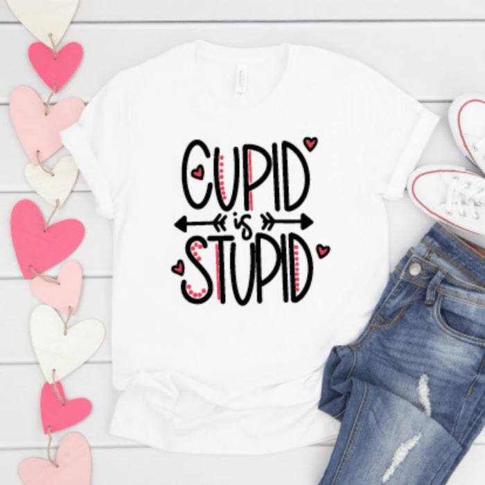 Cupid is Stupid SVG designon white tshirt with jeans and heart garland in background