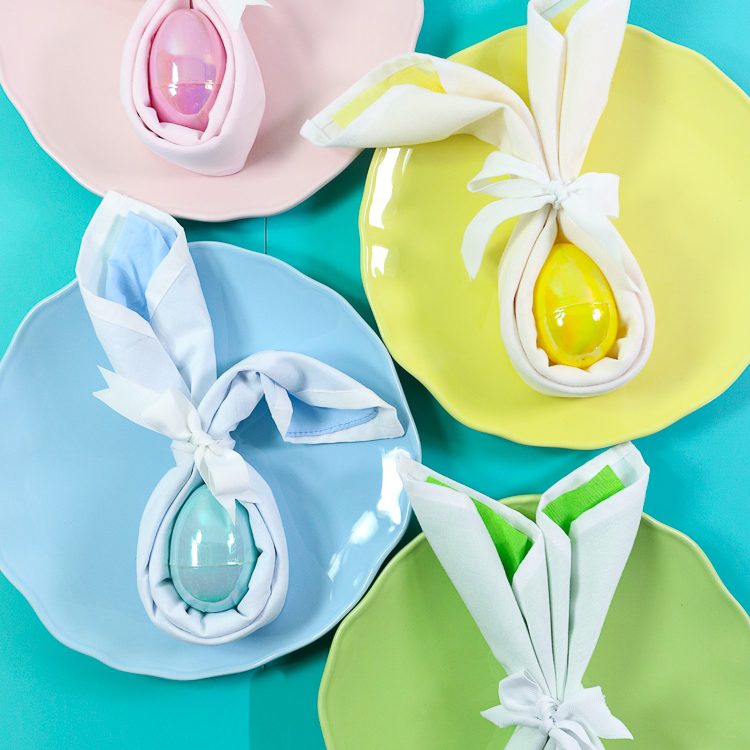 Four pastel plates with matching bunny folded napkins in coordinating colors