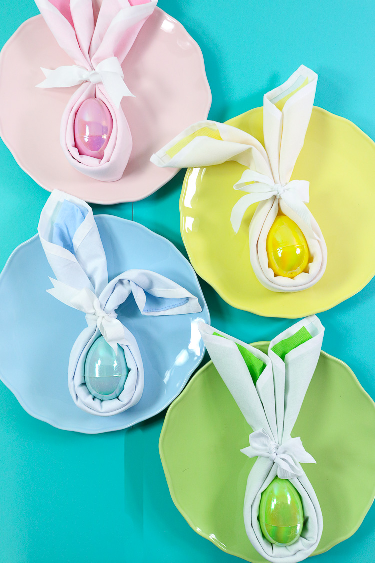 Four pastel plates with matching bunny folded napkins in coordinating colors