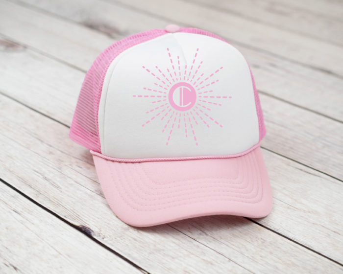 Pink and white trucker hat with single letter monogram set in a sunburst pattern.