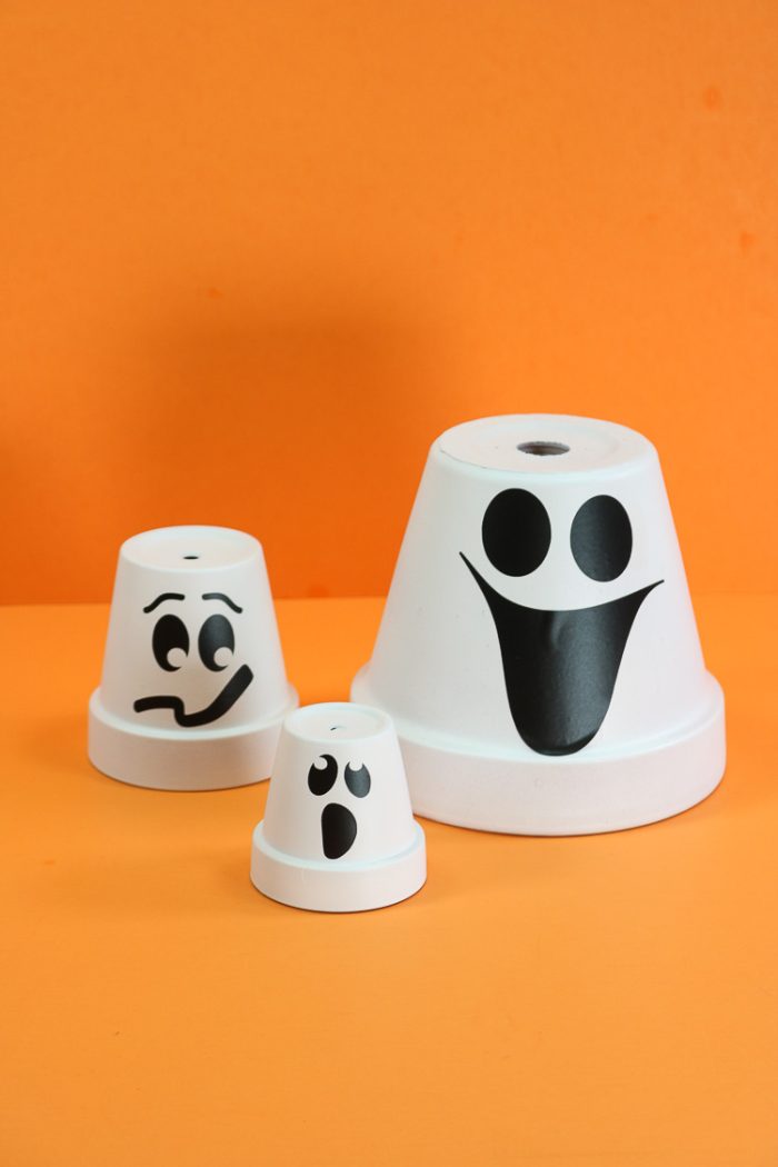 Three terracotta clay pots overturned, painted white and ghost faces added for Halloween decor ideas. 