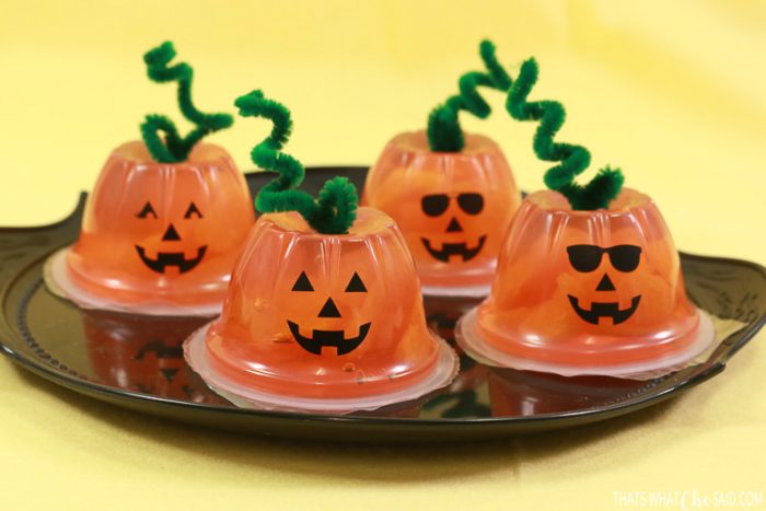 Orange fruit cups turned into jack-o-lanterns with faces and pipe cleaner stems