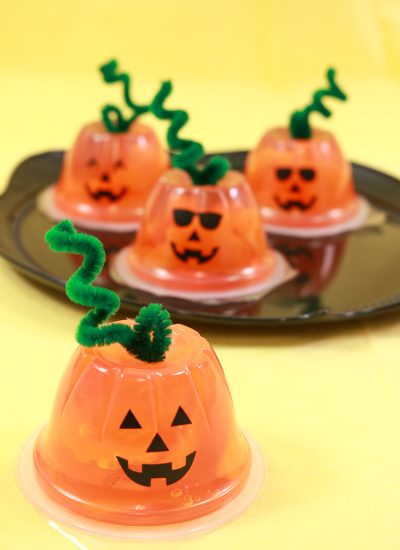 Orange fruit cups turned into jack-o-lanterns with faces and pipe cleaner stems