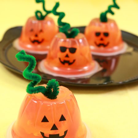 Orange fruit cups turned into jack-o-lanterns with faces and pipe cleaner stems