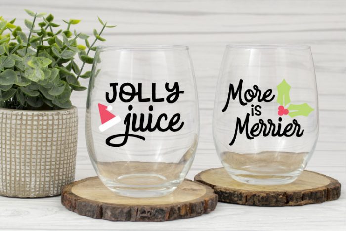 Two clear stemless wine glasses with holiday SVG cut in adhesive vinyl.  One says "Jolly Juice" and the other says "More is Merrier"