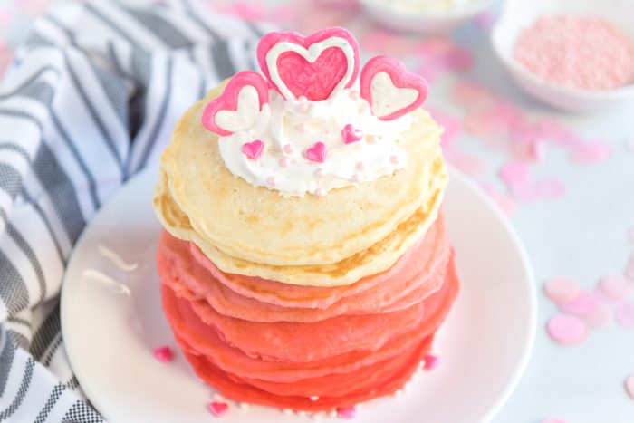 Ombre Valentine Pancakes Stacked on a plate with chocolate candy melt heart design on top with whipped topping. 