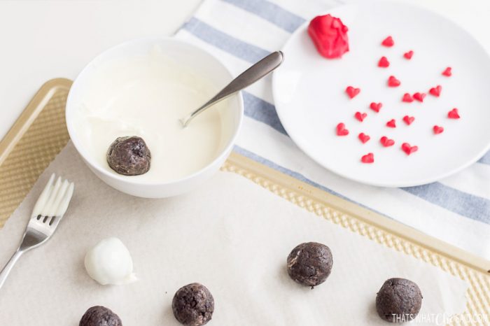 Truffles being dipped into a bowl of melted white chocolate.