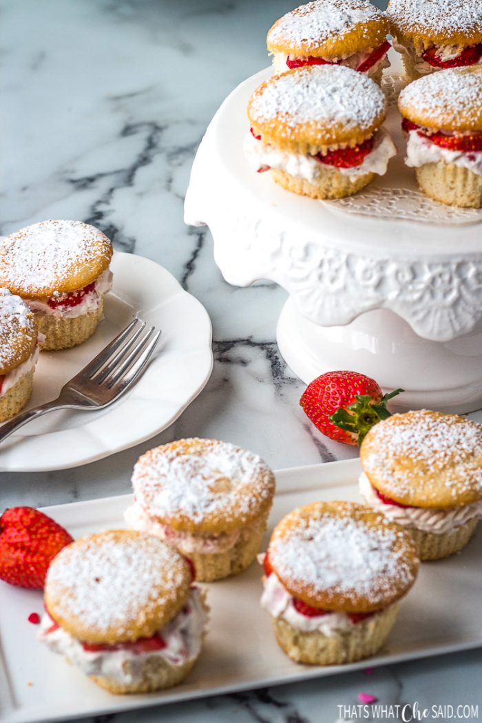 Finished strawberry shortcake cupcakes on a rectangle platter, small plate and cake plate ready for brunch