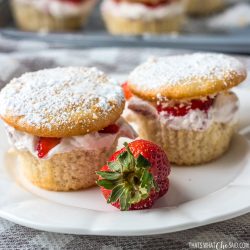 Plate with 2 White cupcakes with tops cut off, strawberry cream added and tops returned with a powdered sugar dusting.