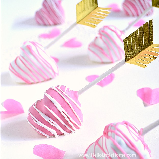 heart shaped cake pops covered in pink icicng and an arrow feathers on teh stick