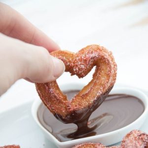 heart shaped churro being dipped in chocolate sauce