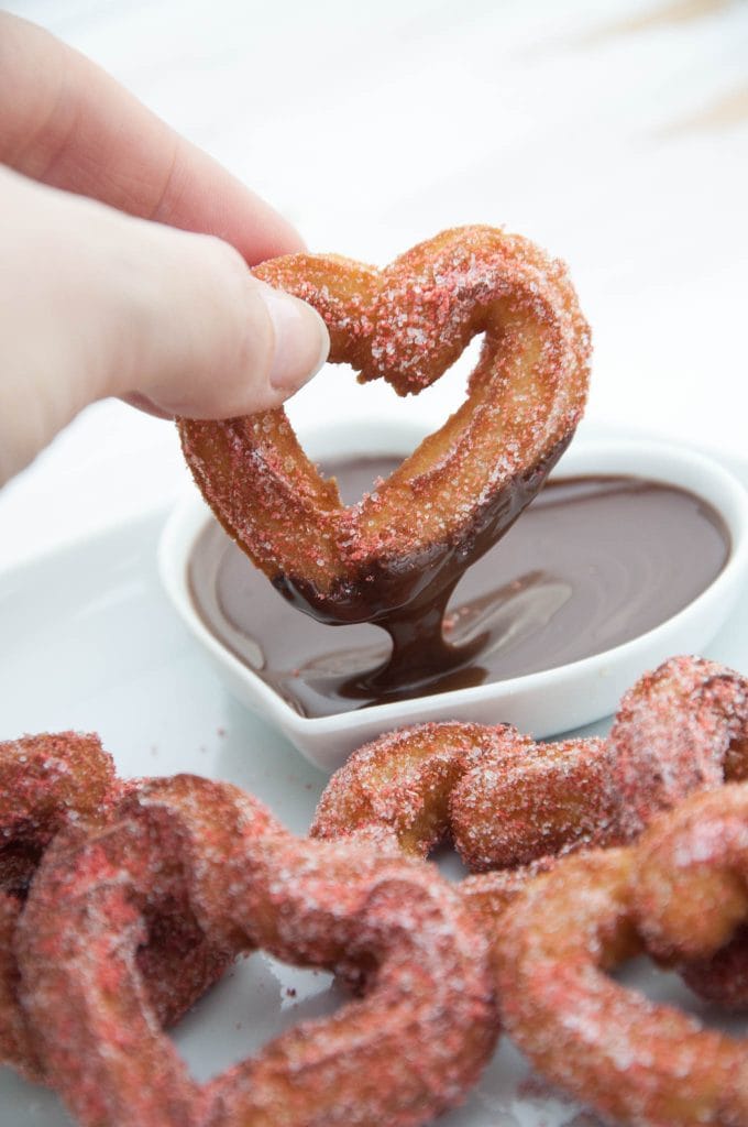 heart shaped churro being dipped in chocolate sauce
