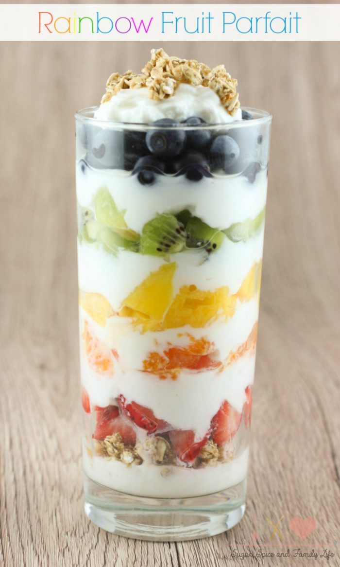 Tall Glass with Layers of fruit and yogurt in rainbow order. Strawberries, oranges, mango, kiwi and blueberries in glass to show rainbow parfait