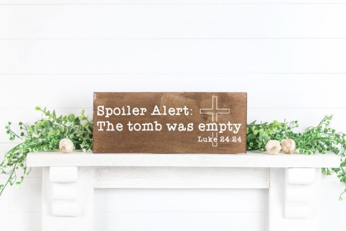White mantel with greenery and flowers and a wooden sign. Easter religious svg in white on the sign
