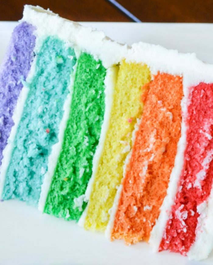 Cake in rainbow layers with white buttercream icing in between the layers and outside the cake