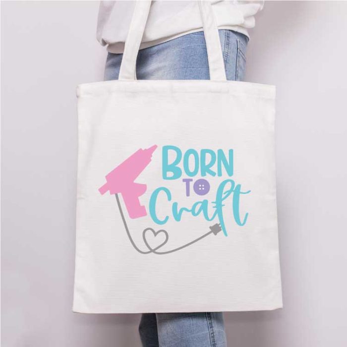 Square - Close up of someone holding a canvas tote with the "born to craft" svg design with glue gun applied in iron vinyl