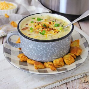 Cheeseburger Soup in a camp mug on a buffalo check plate with croutons