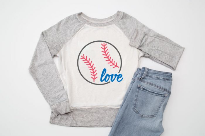 Raglan sweatshirt with grey sleeves and white body with Baseball Love SVG design staged next to a pair of jeans