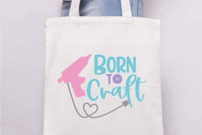 Close up of someone holding a canvas tote with the "born to craft" svg design with glue gun applied in iron vinyl