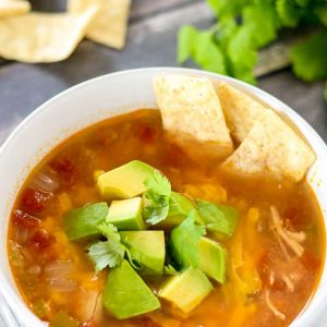 Chicken Tortilla soup with avocado and cilantro garnish with some tortilla strips on the side.