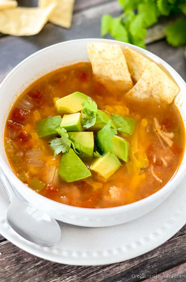 Chicken Tortilla soup with avocado and cilantro garnish with some tortilla strips on the side.