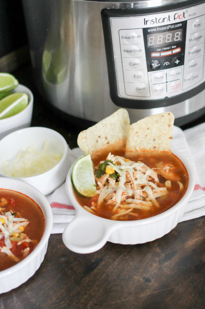 Chicken Tortilla soup with instant pot, limes and cheese in background