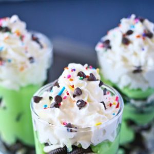 Layered green shooters with whipped topping and rainbow sprinkles