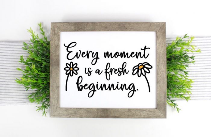 Farmhouse sign on greenery on a table runner with Every Moment is a fresh beginning in vinyl