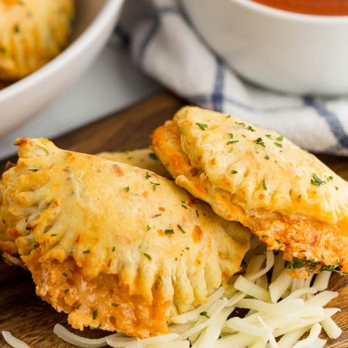 Pizza calzones plated with cheese and a side of red dipping sauce.