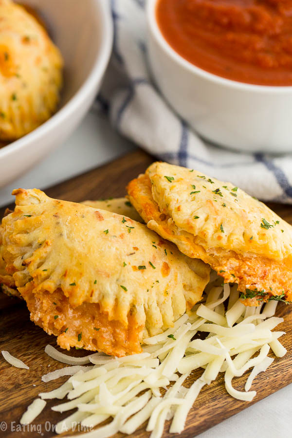 Pizza calzones plated with cheese and a side of red dipping sauce.