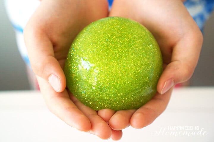 Hands holding a ball of green sparkly slime.