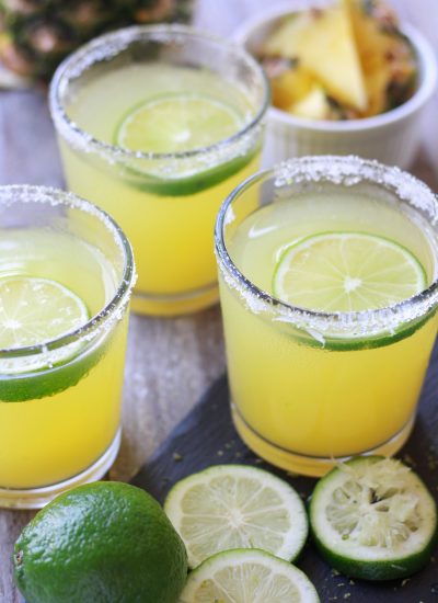 Three Pineapple Margaritas with sliced limes and fresh cut pineapple