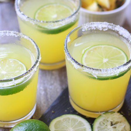 Three Pineapple Margaritas with sliced limes and fresh cut pineapple