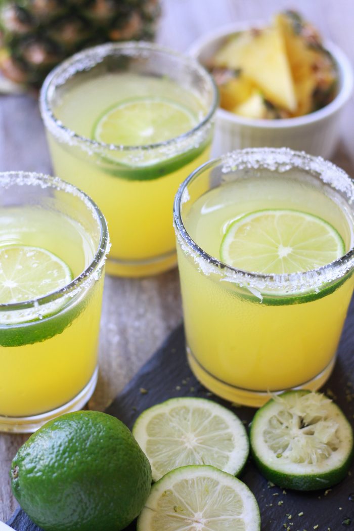 Three Pineapple Margaritas with sliced limes and fresh cut pineapple