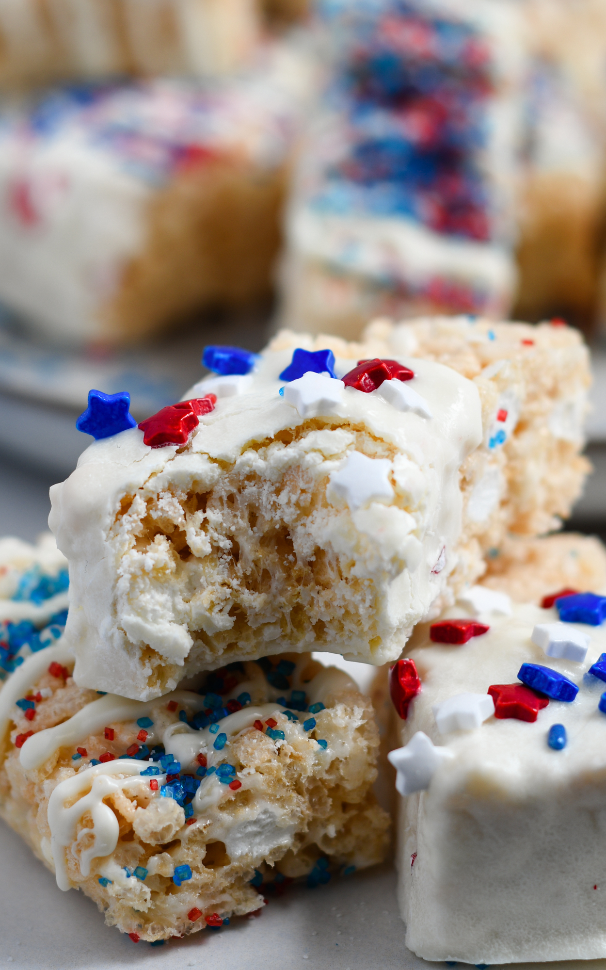 Rice Krispie Treats dipped in white chocolate with red white and blue and stars sprinkles. One has bite from it.