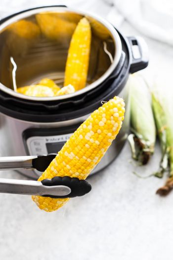 tongs hoding single ear of corn while rest are in the instant pot in background