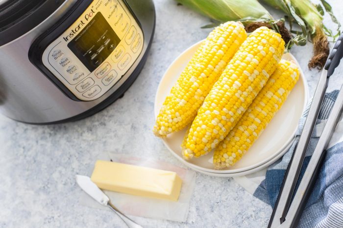 Corn on the cob on a plate with butter and instant pot in background horizontal