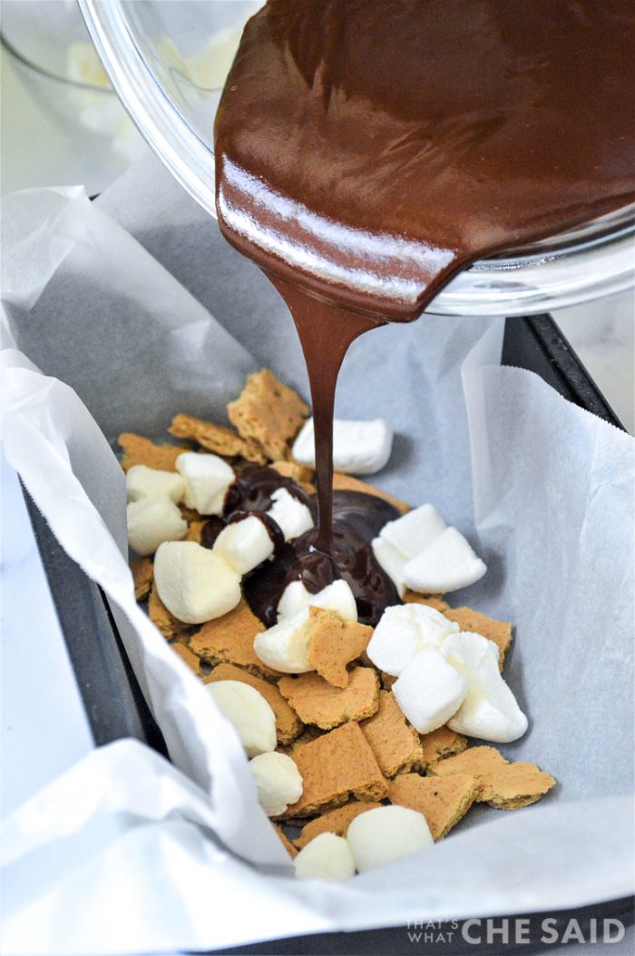 Pouring melted chocolate over marshmallow and graham cracker pieces in parchment lined loaf pan